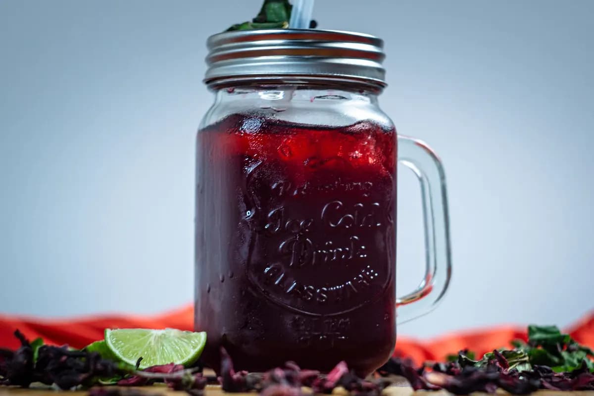 Un bocal de jus d'hibiscus (bissap) frais, avec des fleurs séchées et un quartier de citron vert