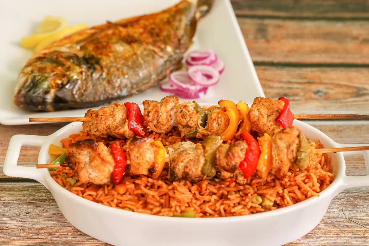 Un plat de riz rouge servi avec du poisson grillé, des brochettes et des légumes
