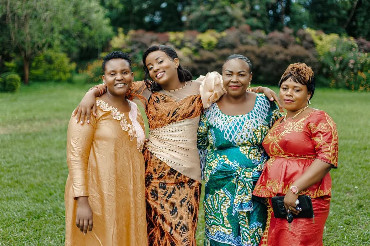 Quatre femmes africaines en tenues colorées, souriantes et enlacées dans un jardin